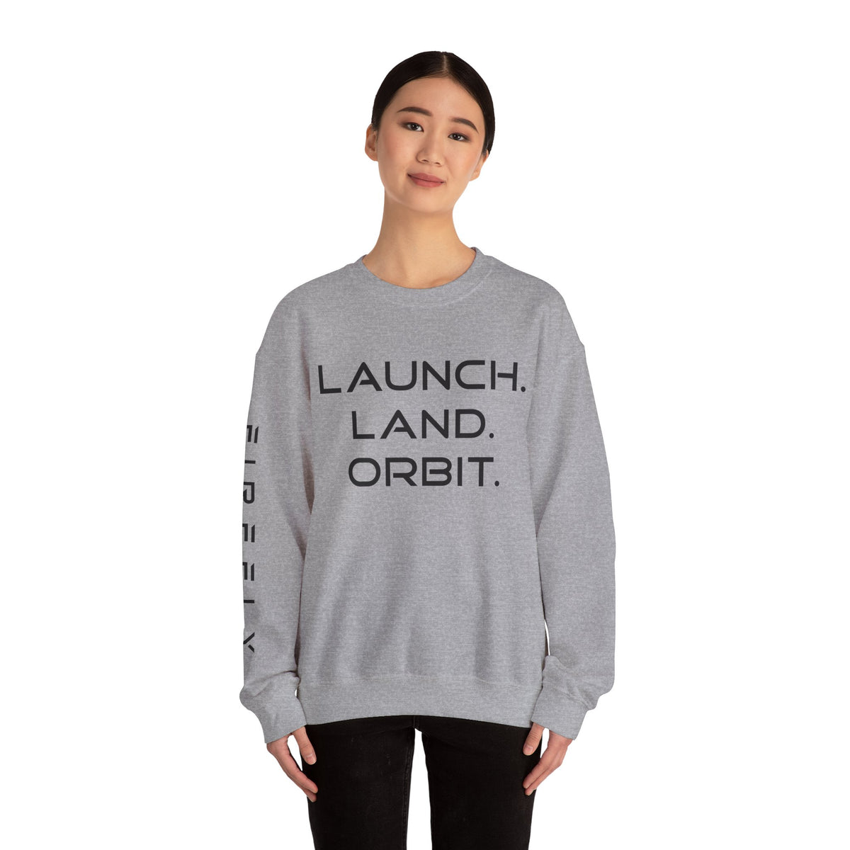 A woman modeling a light gray crewneck sweatshirt with the words 'LAUNCH. LAND.
