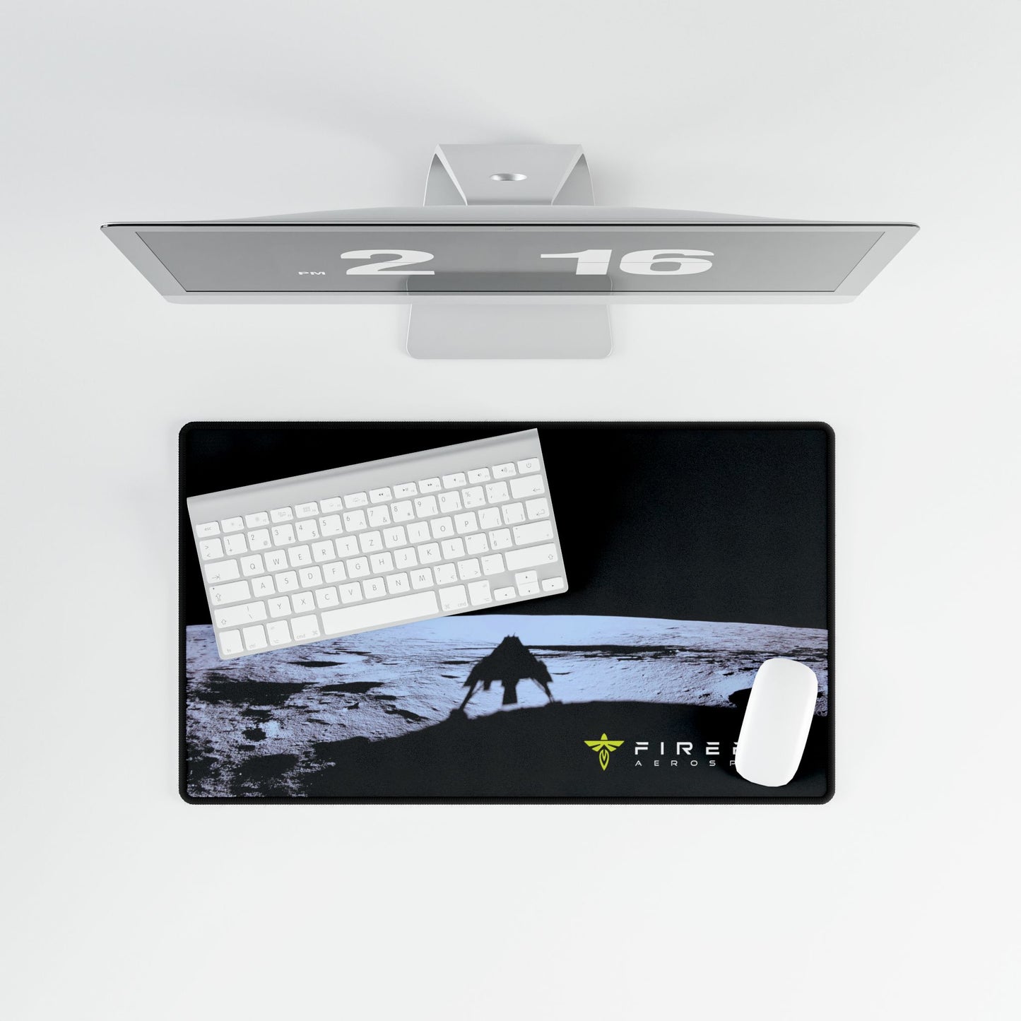 A rectangular desk mat with a black background and a graphic of a creature on a moon-like surface, shown with a white keyboard and mouse on top. A sleek silver monitor is positioned above the desk mat against a clean white background.
